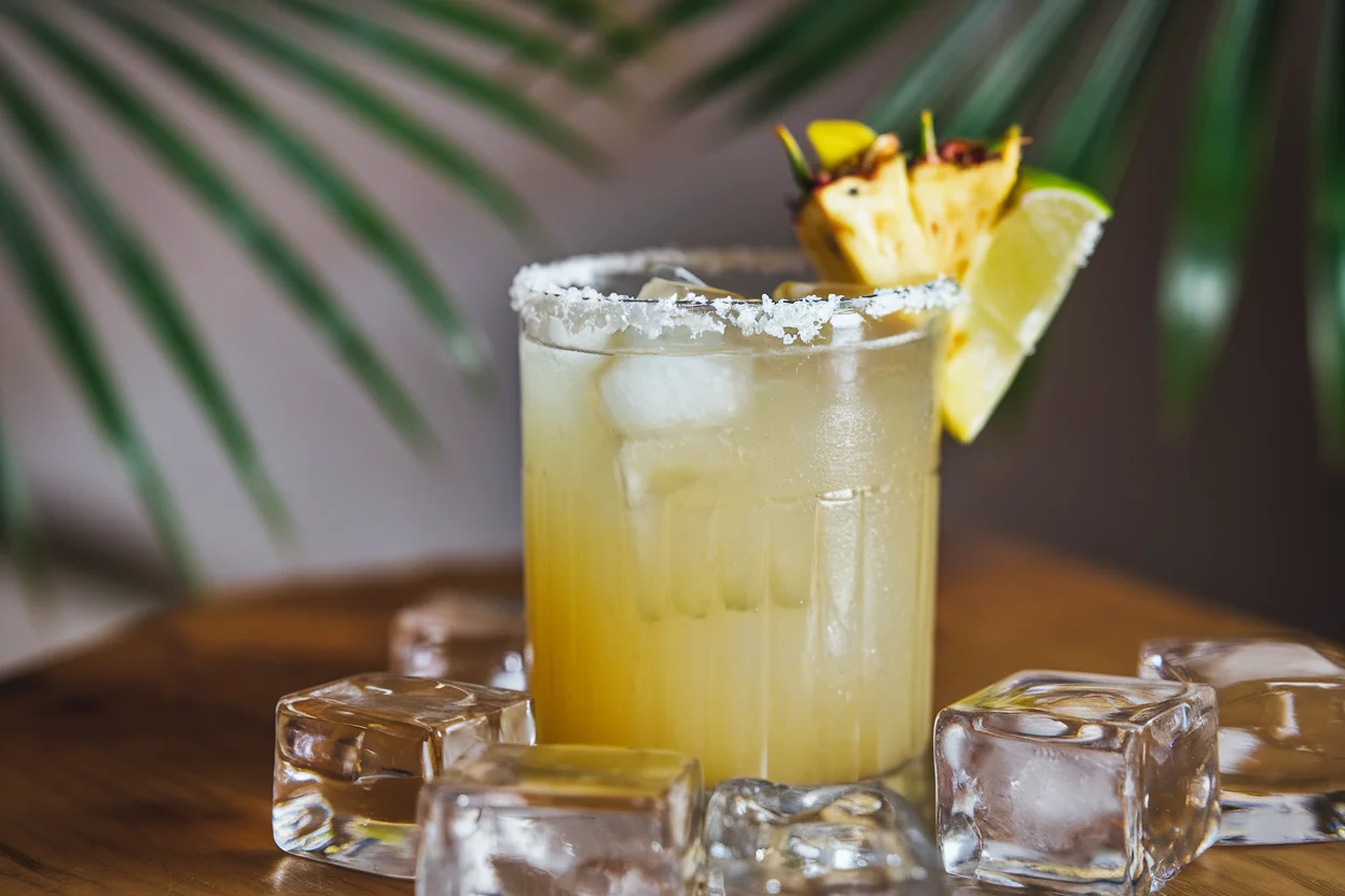 Final presentation of a pineapple margarita recipe, featuring a tall glass with a salted rim, fresh pineapple garnish, and lime wedge.